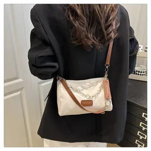 Détail d'un sac bandoulière beige minimaliste avec chaîne florale sur un blazer noir