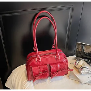 Detail of red patent leather shoulder bag with decorative bows and glossy finish