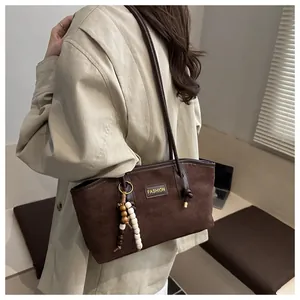 Detalle de bolso bandolera de ante marrón oscuro con etiqueta de moda y colgante de cuentas