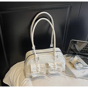 Detail of creamy white patent leather shoulder bag with decorative bows and twin handles