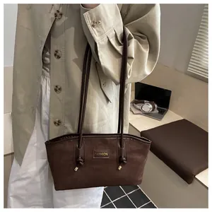 Detalle del bolso tote de ante marrón oscuro con placa dorada y correas con nudos