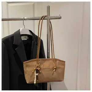 Detalle de bolso tote de ante marrón con placa FASHION y colgante de cuentas decorativas