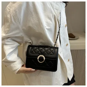 Détail d'un sac bandoulière noir matelassé avec boucle dorée en perles et chaîne