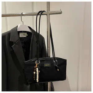 Detalle de bolso tote de ante negro con placa dorada y colgante de borlas y cuentas