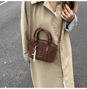 Detalle del bolso tote de leopardo con asas de cuero marrón y accesorio de amuleto de cuentas