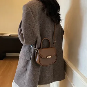 Sacoche marron en cuir pour femme portée en bandoulière sur un manteau élégant