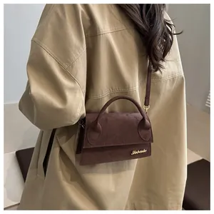 Detail of dark brown suede shoulder bag featuring a minimalist gold logo and soft texture