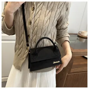 Detail of black matte mini crossbody bag with golden logo and slender shoulder strap