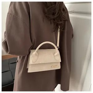 Chic beige suede crossbody bag with gold logo shown on model with dark coat