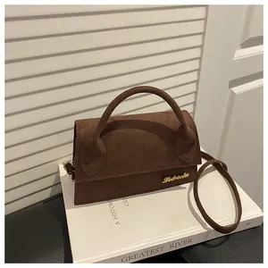 Close-up of dark brown suede handbag with golden metal logo and fine matte texture