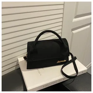 Detail of matte black suede crossbody bag with gold logo on white decorative background