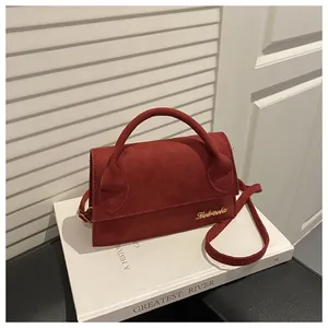 Detailed macro view of a red suede crossbody bag with elegant gold logo and handle