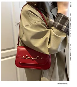 Detail view of red faux leather shoulder bag with golden horsebit buckle on khaki coat