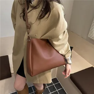 Vintage brown leather bucket bag with silver studs worn by a model in khaki trench coat