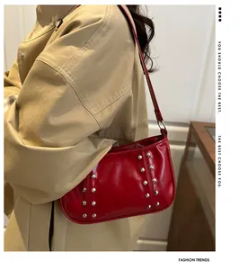 Close-up of red patent leather shoulder bag with silver stud rivets on beige jacket