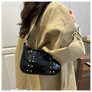 Detail of black glossy patent leather shoulder bag with silver studs on a female model