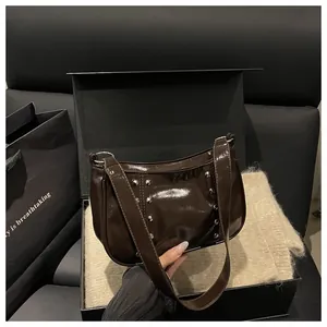Detailed view of dark brown glossy patent leather shoulder bag with silver metal rivets