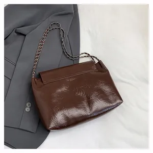 Detail view of brown glossy leather tote bag with silver chain strap on grey blazer