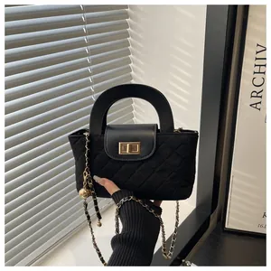 Detail of black quilted handbag with gold clasp, rigid handle and metallic chain strap