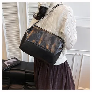 Detail view of the black glossy wrinkled leather texture and metallic chain strap of the bag