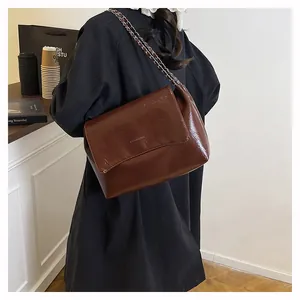 Detail view of large brown glossy tote bag with chain strap and embossed fashion text