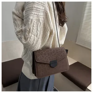 Détail du sac à bandoulière léopard avec boucle noire sur un pull en tricot blanc