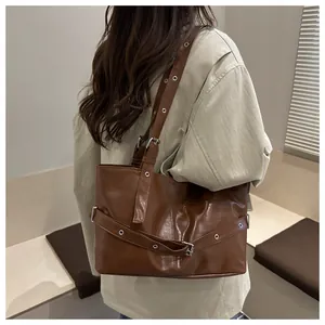 Detalle del bolso de hombro en ecocuero marrón con ojales metálicos y hebilla decorativa