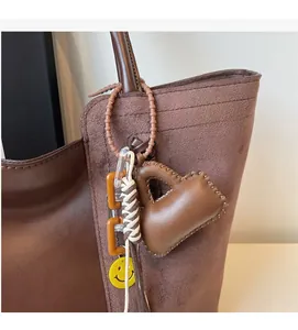 Dettaglio del ciondolo in pelle marrone con cuciture fini e tag smiley su una borsa tote