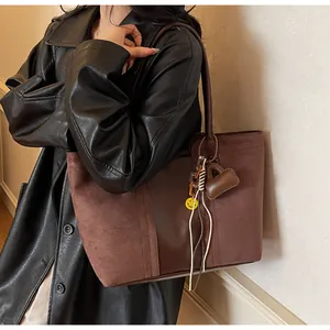 Dettaglio della borsa tote marrone scuro con contrasto scamosciato e ciondolo smiley giallo
