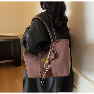 Dettaglio di una borsa tote in pelle scamosciata marrone con ciondolo smiley e frange