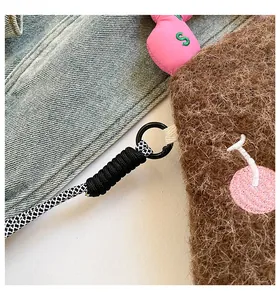 Dettaglio della borsa in peluche marrone con ciondolo a ciliegia e tracolla a scacchi