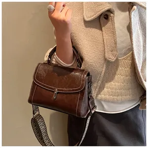 Detail of vintage brown crossbody bag featuring contrast stitching and woven strap