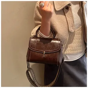 Detail of dark brown leather handbag with contrast stitching and woven geometric strap