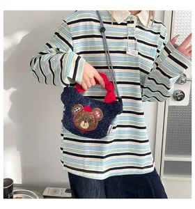 Dettaglio borsa di peluche blu con ricamo orsetto e manici ondulati rossi su modella