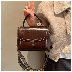 Detailed view of brown leather bag with white contrast stitching and wide woven strap