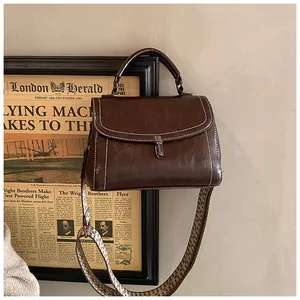 Detail of dark brown leather crossbody bag featuring white stitching and geometric strap