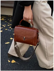 Detail of vintage brown crossbody bag featuring contrast stitching and geometric woven strap