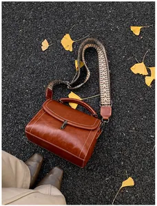 Close-up of brown vintage leather crossbody bag with white stitching and wide woven strap