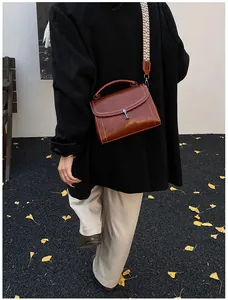 Brown retro crossbody bag with geometric woven strap on autumn ginkgo leaves background