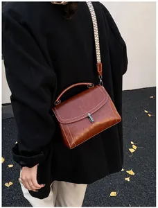 Detail of vintage brown leather crossbody bag with woven strap on an autumn background