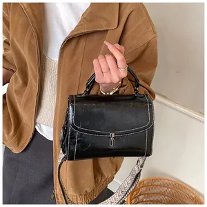 Detail of black leather crossbody bag with white stitching and decorative woven strap