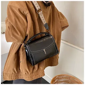 Detail of black glossy handbag featuring white contrast stitching and jacquard strap