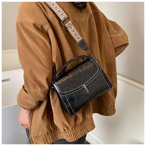 Detail of a black crossbody bag with white stitching and a vintage patterned wide strap