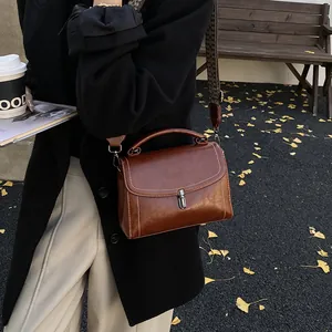 Retro dark brown crossbody bag with wide strap and white stitching on a park bench