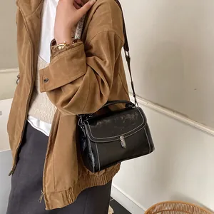 Retro black leather crossbody bag with white stitching and silver clasp on a model