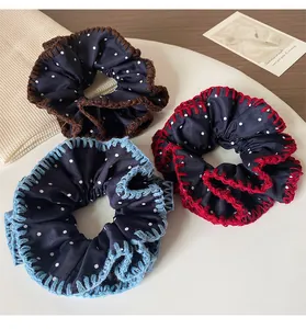 Detailed view of three polka dot denim blue scrunchies with colorful stitching in a tray