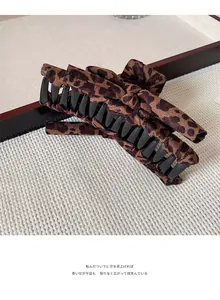 Close-up of leopard print bow hair claw clip on textured woven mat with warm lighting