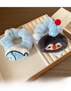 Close-up of plush penguin and fish charm hair scrunchies on a wooden tray