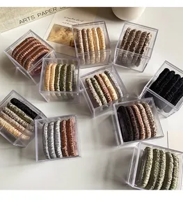 Close-up of satin hair scrunchies set in earthy tones inside a clear acrylic box