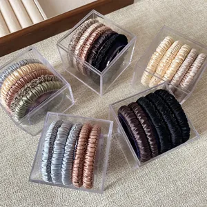 Elegant satin hair scrunchies set in various muted colors inside a clear acrylic box